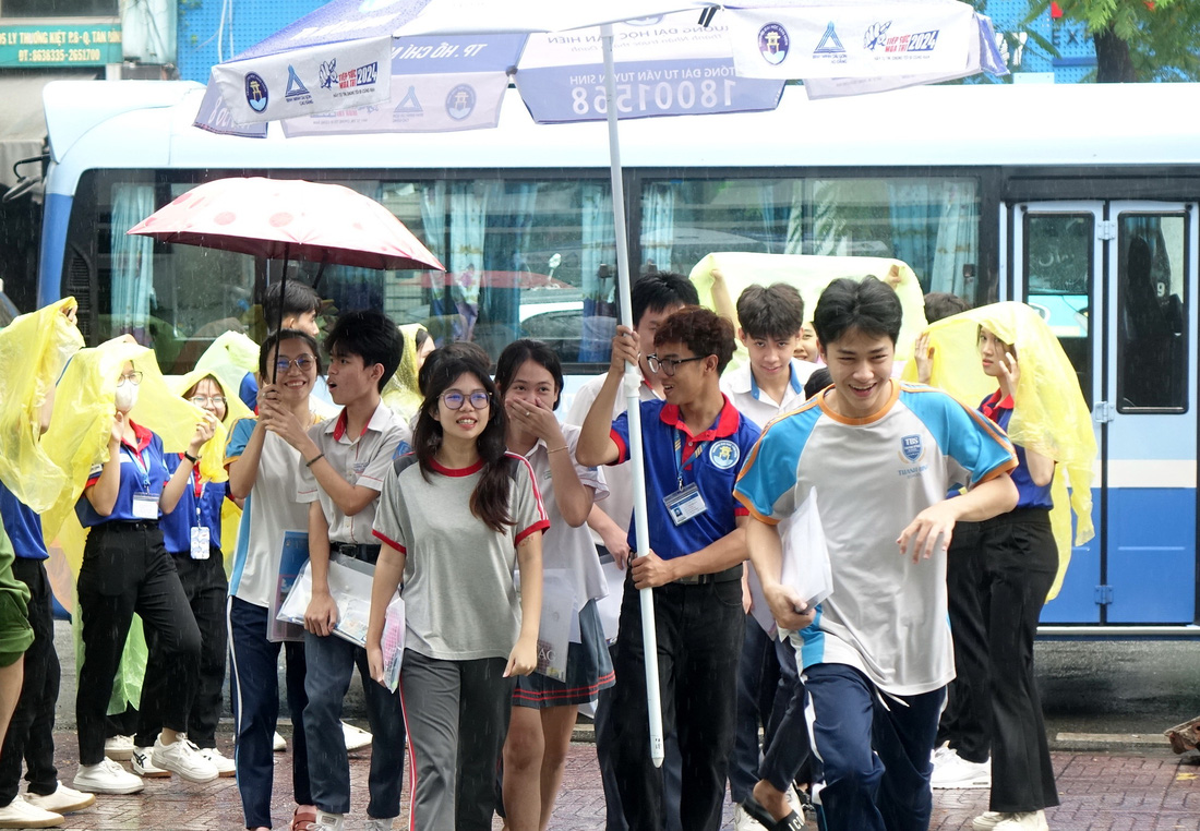 Sinh viên tình nguyện che mưa cho thí sinh vào điểm thi chuẩn bị cho bài thi môn Toán tại điểm thi Trường THCS Nguyễn Gia Thiều, Q.Tân Bình, TP.HCM - Ảnh: NHƯ HÙNG